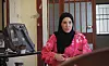 Kvinne i svart hijab og rosa plagg sitter ved et skrivebord i et rom med vinduer.