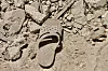 En slitt sandal ligger blant steiner og grus.