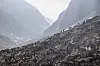 Ponnier og hester samlet i en bratt, steinete fjellside i en smal fjelldal.