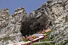 Inngangen til Amarnath-grotten i en bratt fjellvegg, med røde rekkverk og fargerike flagg.