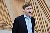 Åsmund Aukrust i mørk dress foran en vegg med lyst treverk.