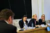 Tre kvinner sitter ved et panelbord med mikrofoner og vannflasker.