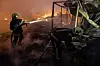 To brannmannskaper arbeider ved en brennende markedsplass i Kyiv, med flammer og røyk i bakgrunnen.