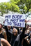 Demonstrant holder en håndskrevet plakat med teksten «My body is not yours to take!» i en folkemengde.
