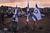 Tre israelske flagg står i et steinete område foran tett boligbebyggelse.